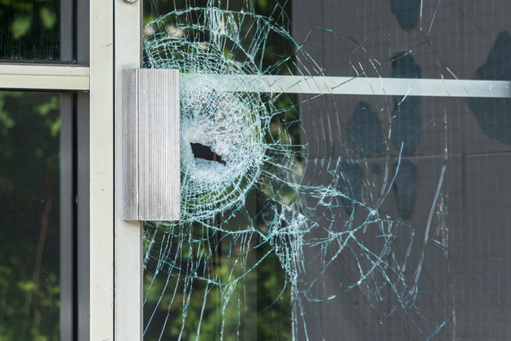 A shattered glass door pane with a hole punched through the centre