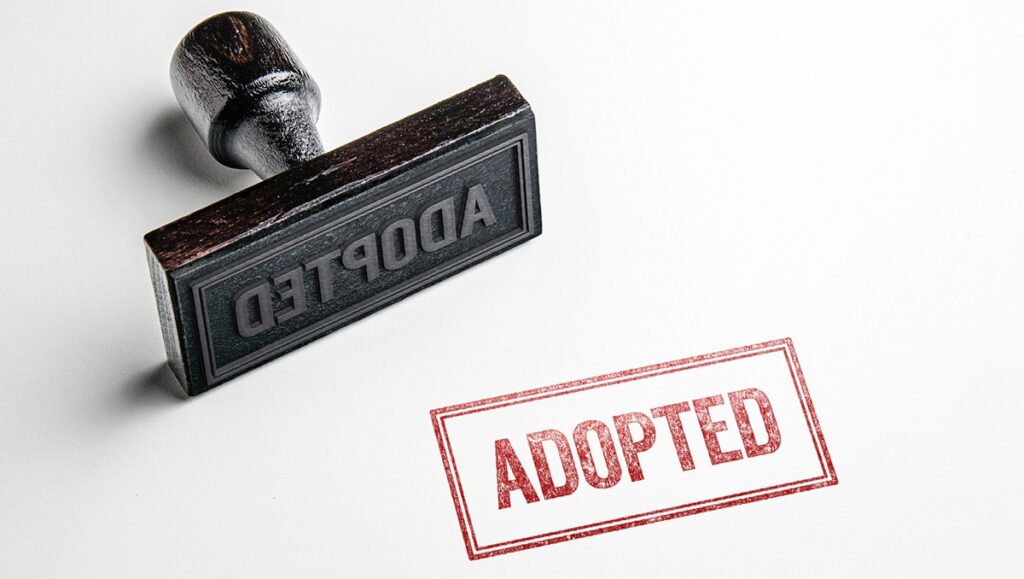 A rubber stamp lying beside the word ADOPTED stamped in red on white paper