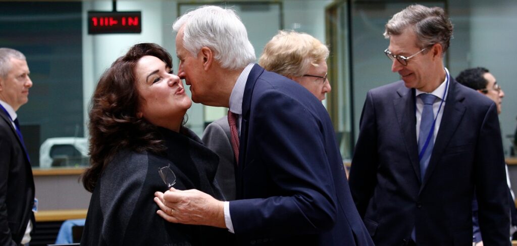 Officials in suits greeting each other with a kiss on the cheek before a meeting in an EU council chamber