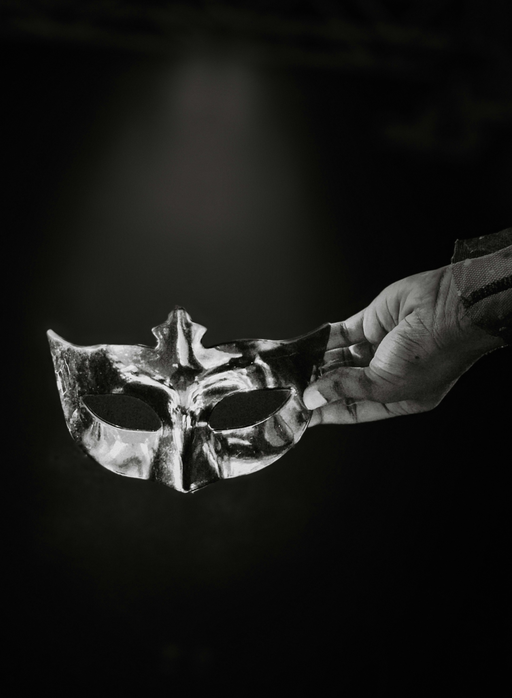 Hand holding up a masquerade mask in the dark