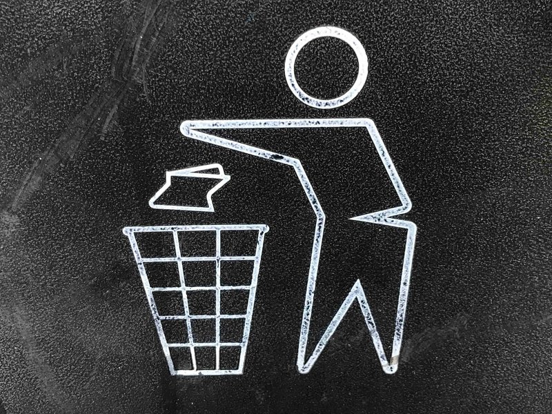 A white outline of a person dropping litter into a bin, painted on a dark surface