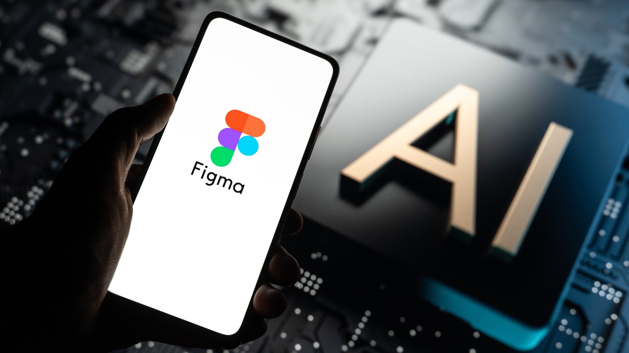 A hand holding a phone with the Figma logo on screen, in front of a chip marked AI