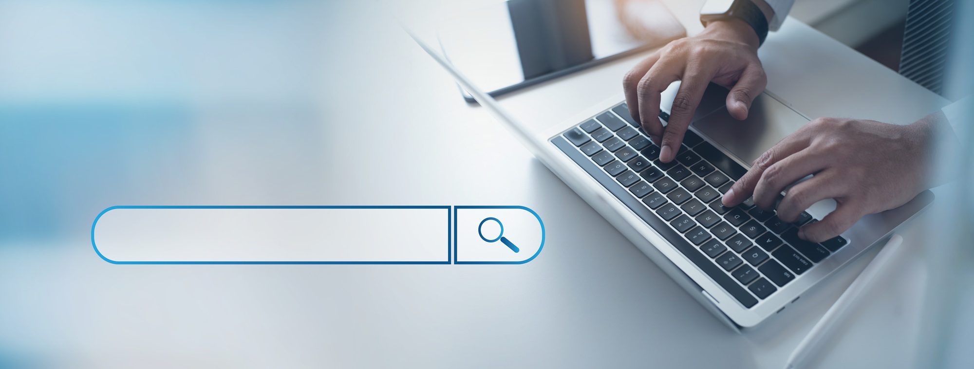 Hands typing on a laptop next to an empty search bar with a magnifying glass icon