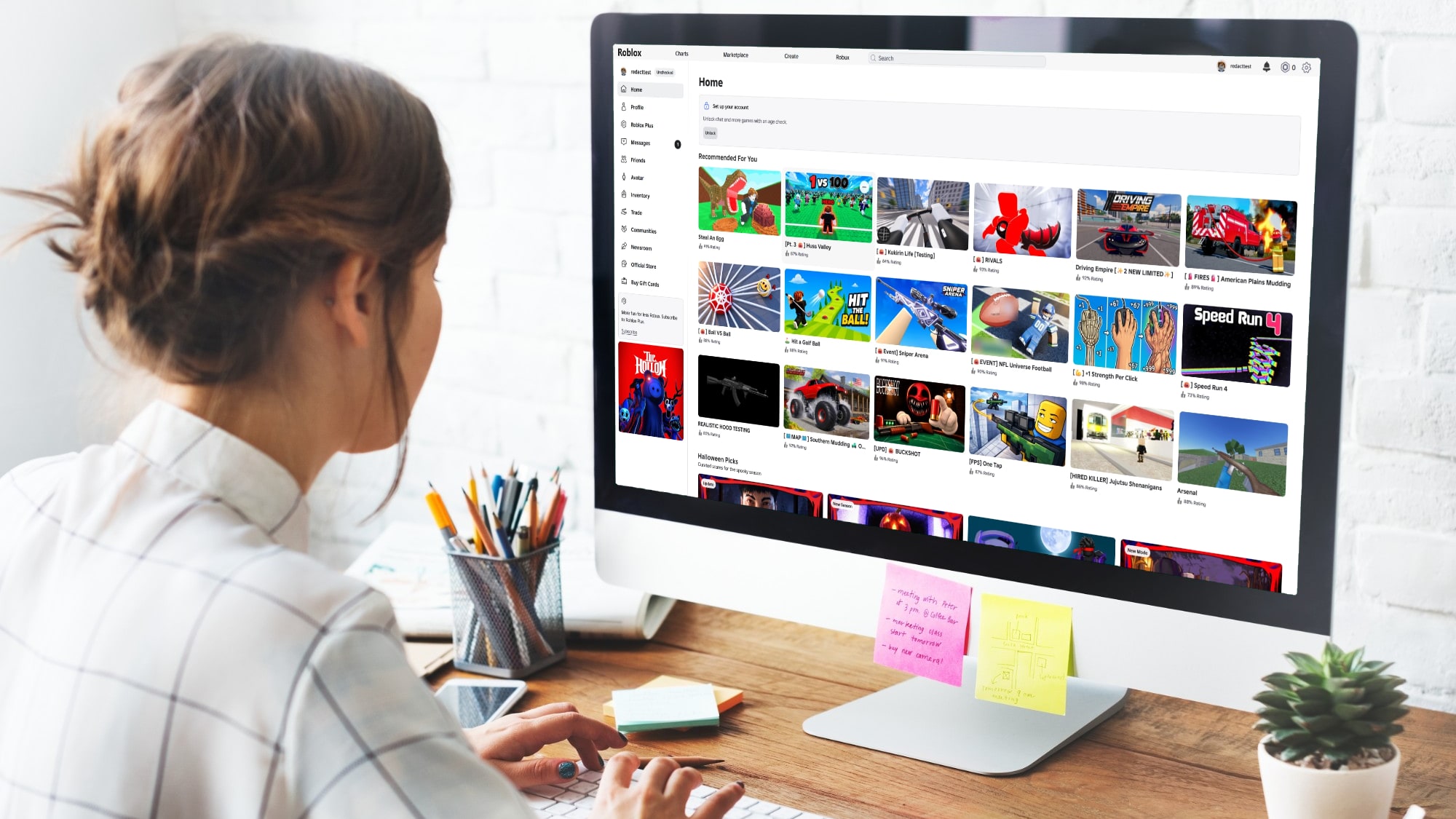 A person at a desk looking at the Roblox home page on a desktop computer